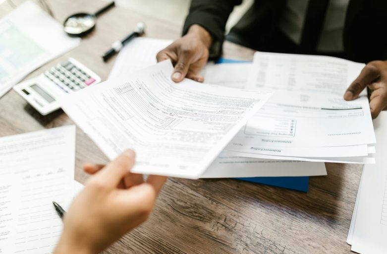 Two professionals exchanging documents in an office setting, focusing on paperwork and data analysis.